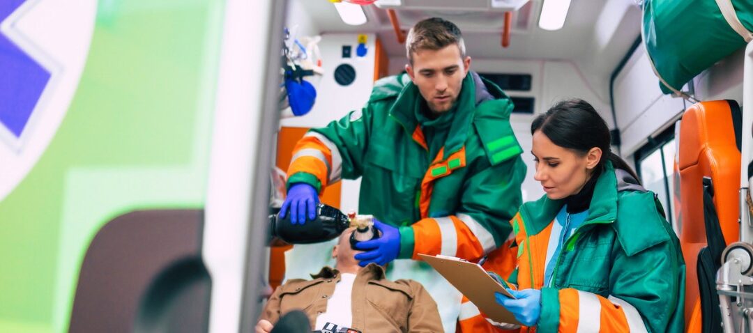 un hombre y una mujer vestidos de sanitarios de verde dentro de una ambulancia atendiendo a un paciente entubado